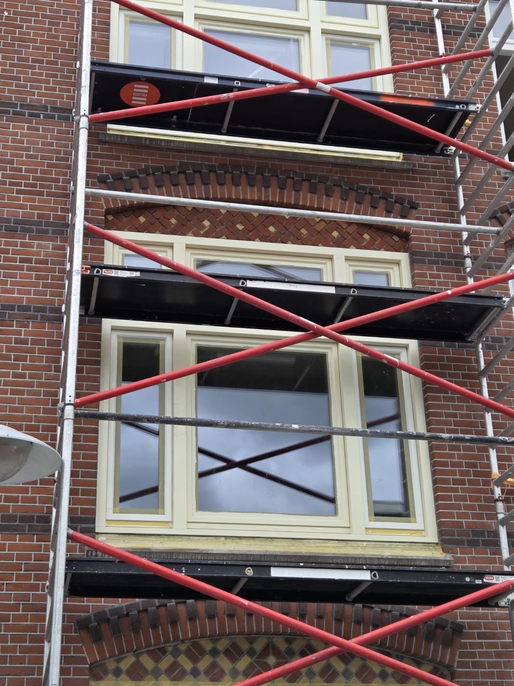 Herstelde bakstenen sierbogen boven de vensters van een jaren-30 gevel, met opnieuw geschilderde kozijnen