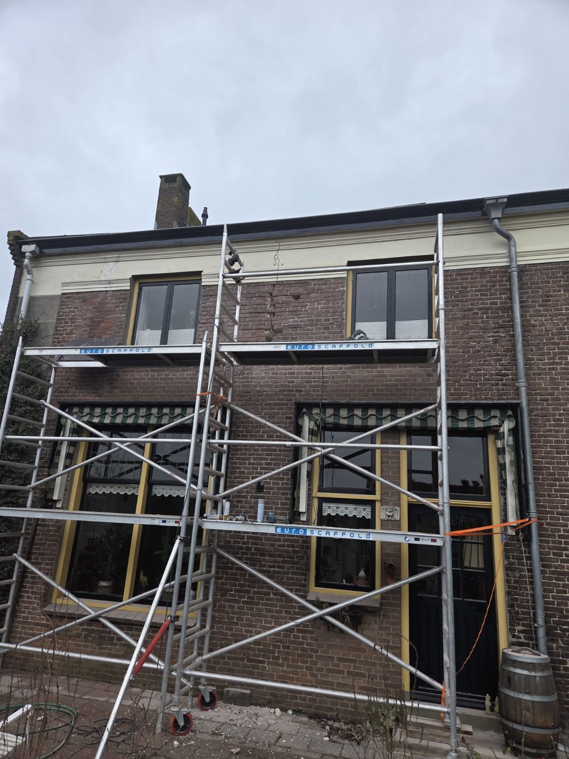 Karakteristieke woning met een rolsteiger tegen de gevel tijdens herstelwerk aan het metselwerk