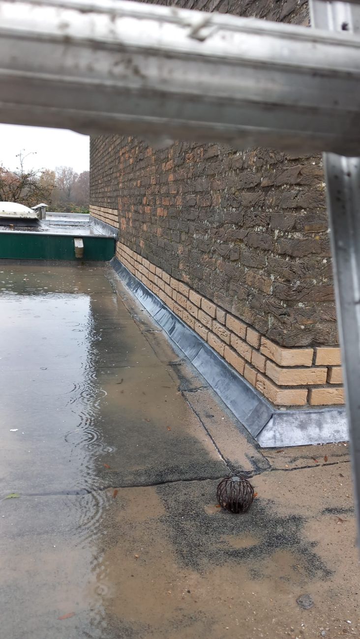 Nieuw aangebracht loodwerk in de aansluiting tussen een bakstenen muur en een plat dak