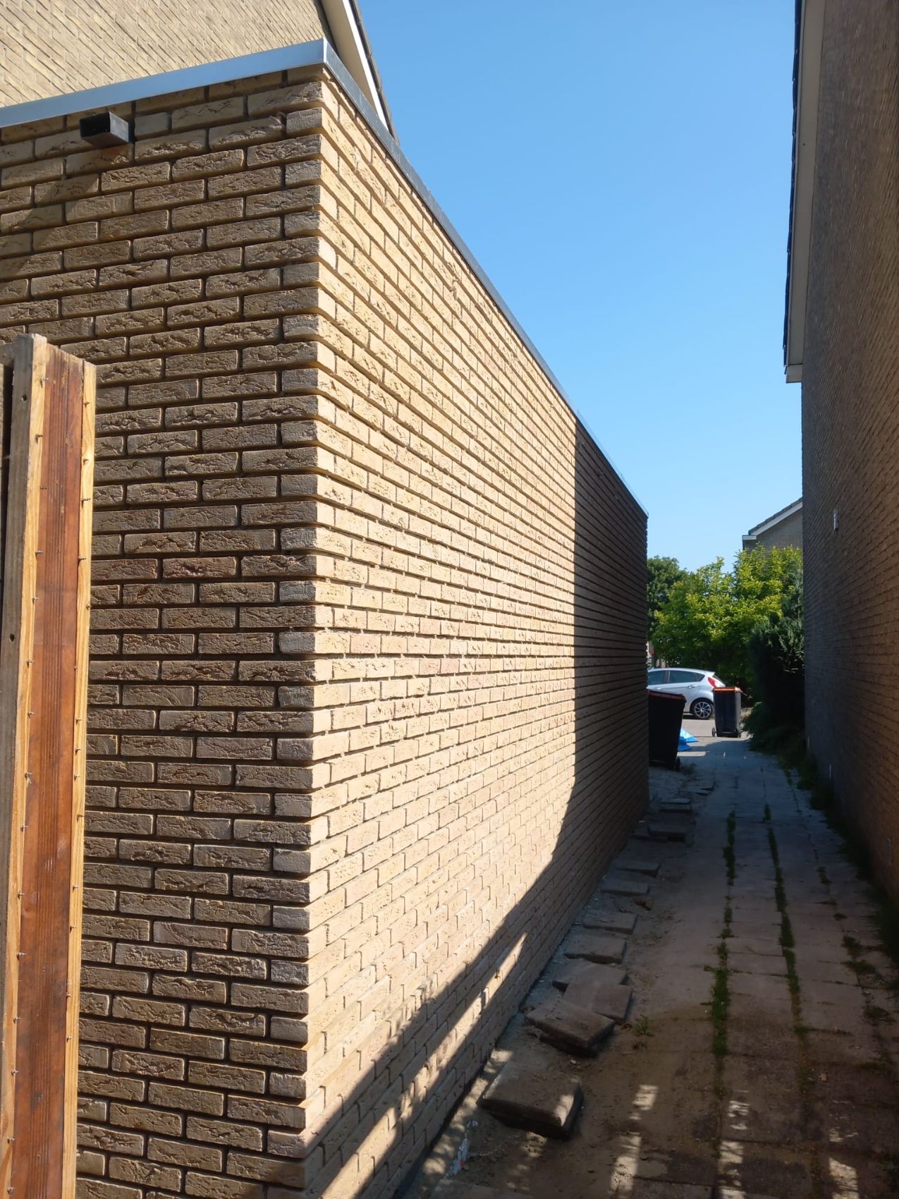 Lange bakstenen muur van een bijgebouw in lichtgele steen, in zonlicht.