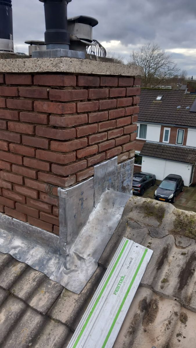 Bakstenen schoorsteen met verweerd voegwerk en oud loodwerk.
